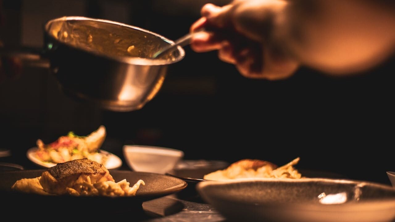 Gourmet dish being plated by a chef in a dimly lit restaurants kitchen.